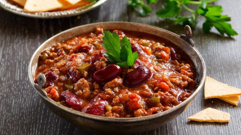 Chili con carne podane w ceramicznej misce, udekorowane czerwoną fasolą i kolendrą