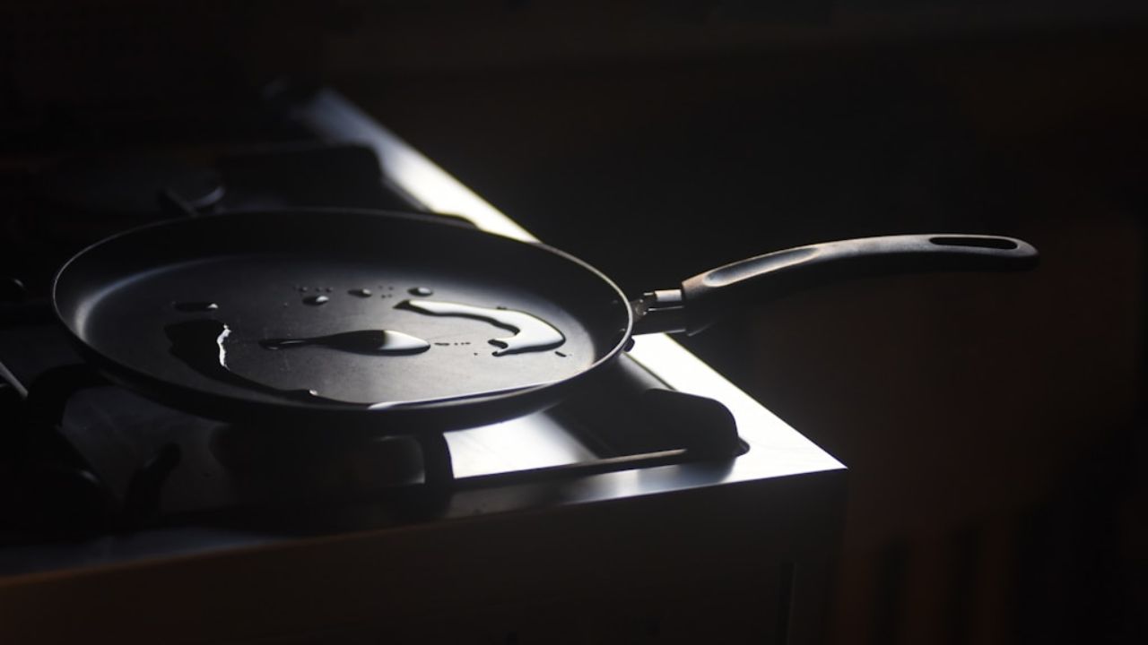 Czarna patelnia z olejem na czarnej płycie z palnikami